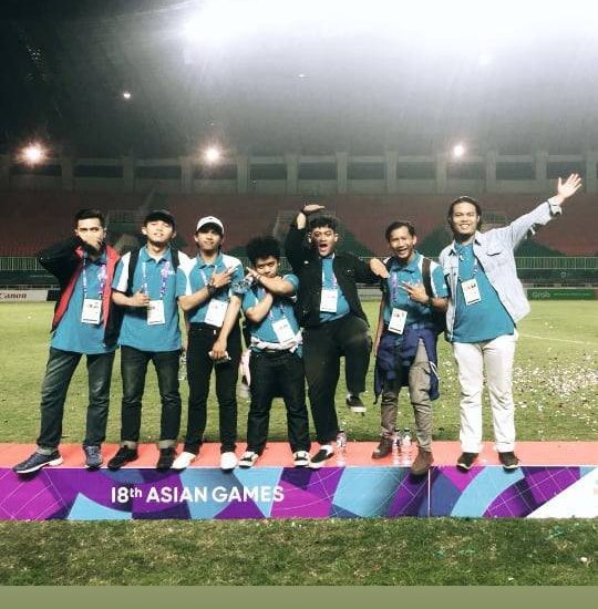 Reva and his team posing on the field at the 18th Asian Games, teal staff shirts and lanyards